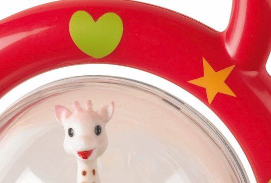 Zbliżenie czerwonego uchwytu grzechotki Sophie la girafe z zielonym sercem i głowy żyrafy w przezroczystej kuli.