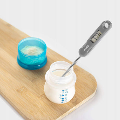 Sonda termometru REER FoodTemp zanurzona w otwartej butelce na mleko.